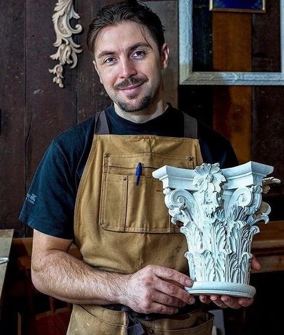 Daniel Ponde in a leather apron in his workshop, holding a white carved Corinthian capital